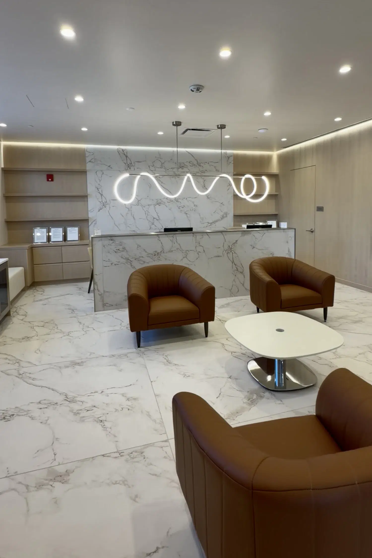 Wide view of COSURGERY waiting area with marble floors, cognac leather chairs, and custom LED lighting.