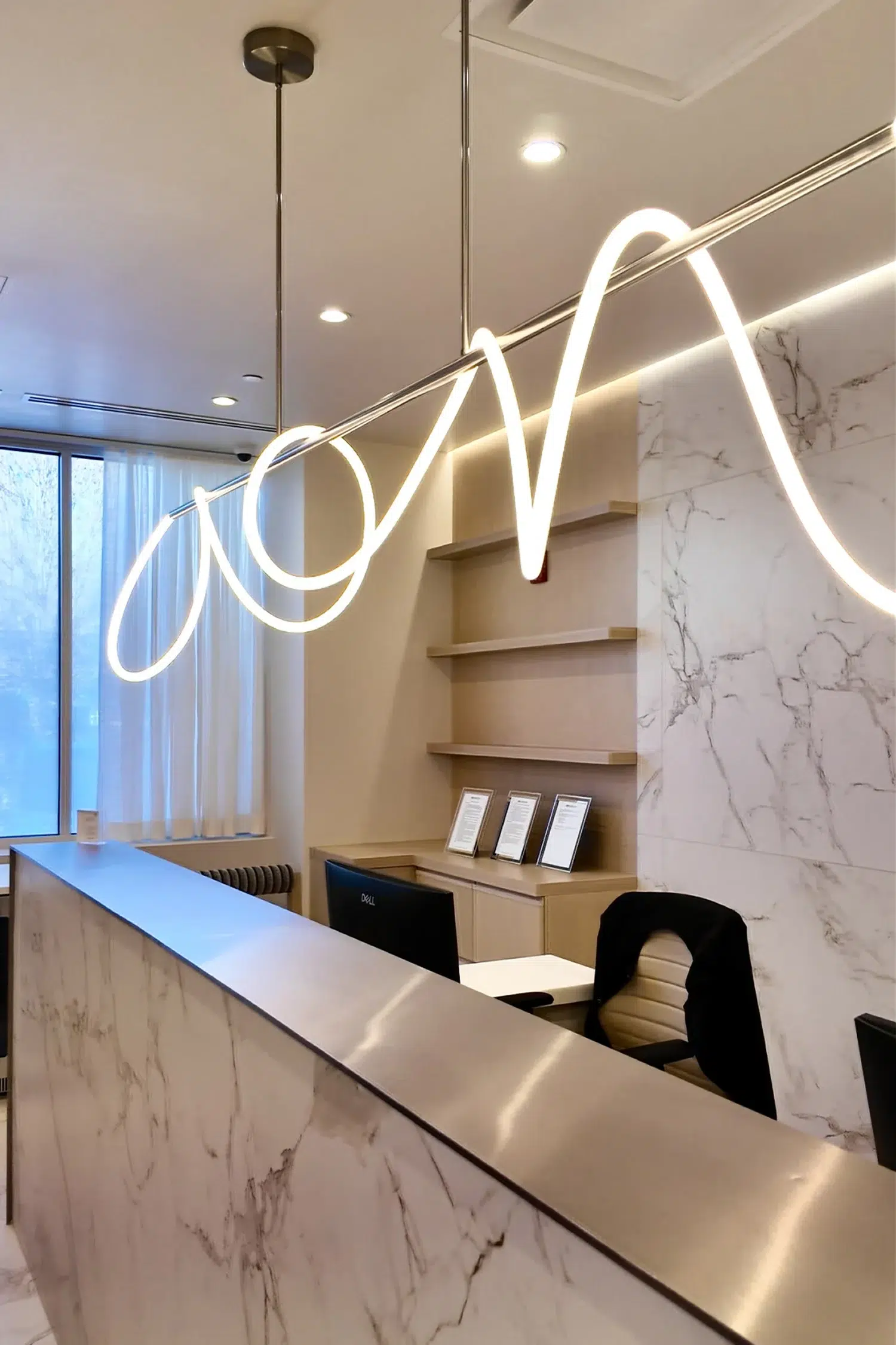 Close-up of marble reception desk at COSURGERY with unique wavy neon light fixture and minimalist decor.