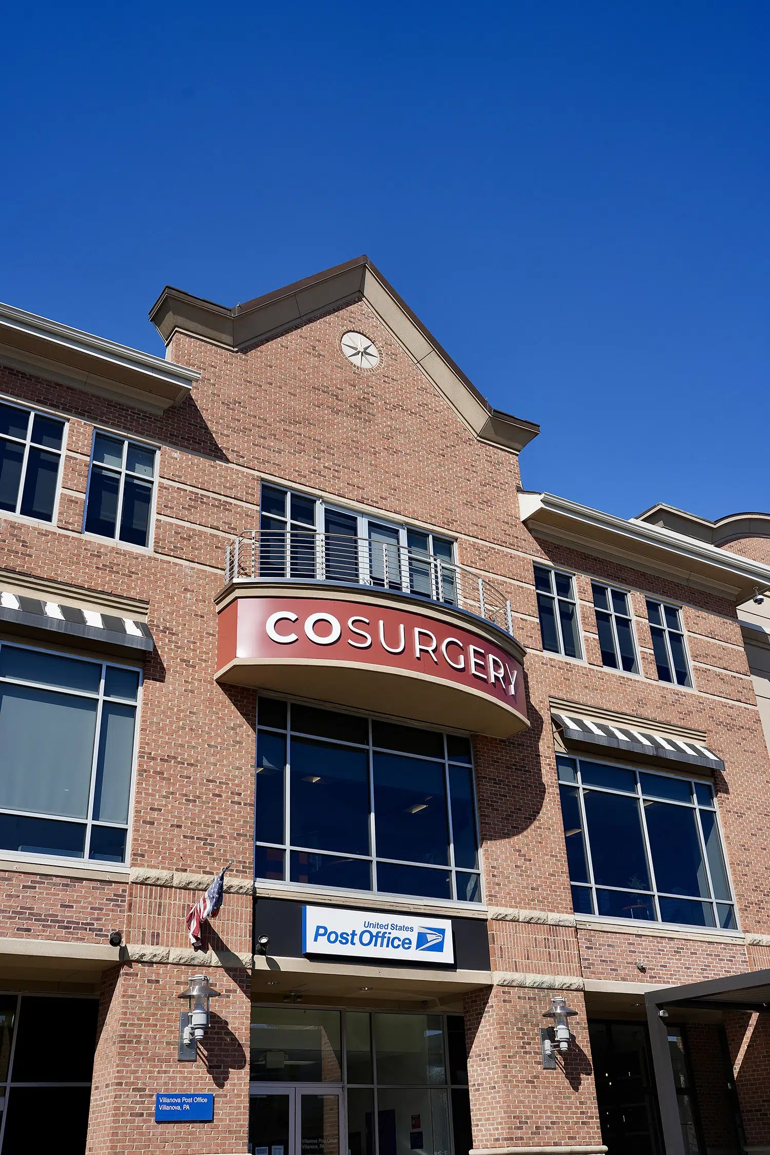 Exterior of COSURGERY plastic surgery center in Villanova, PA, located in a brick building above a US Post Office.