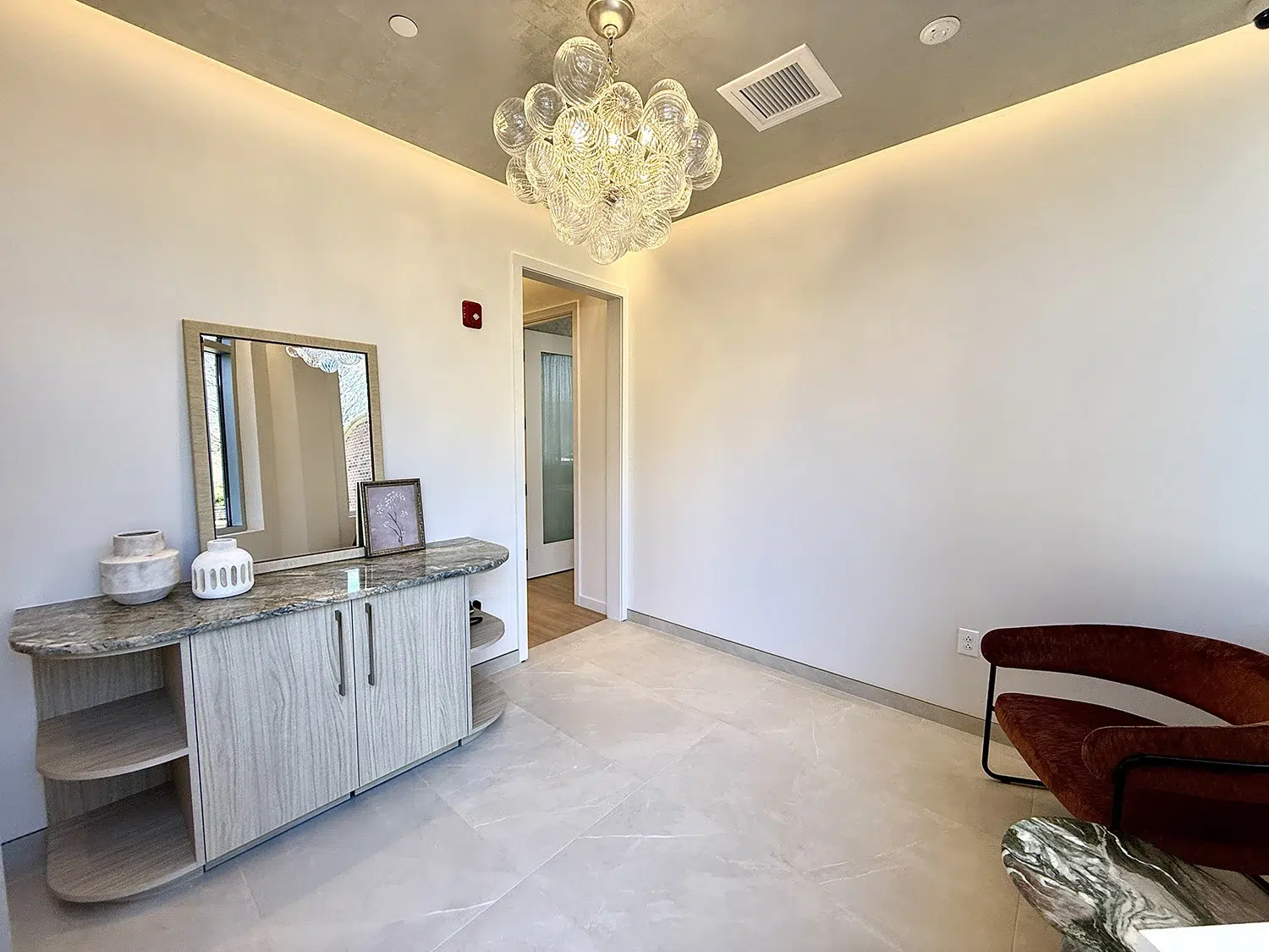 Modern luxury clinic foyer with bubble glass chandelier, marble-top console, and contemporary curved armchair.