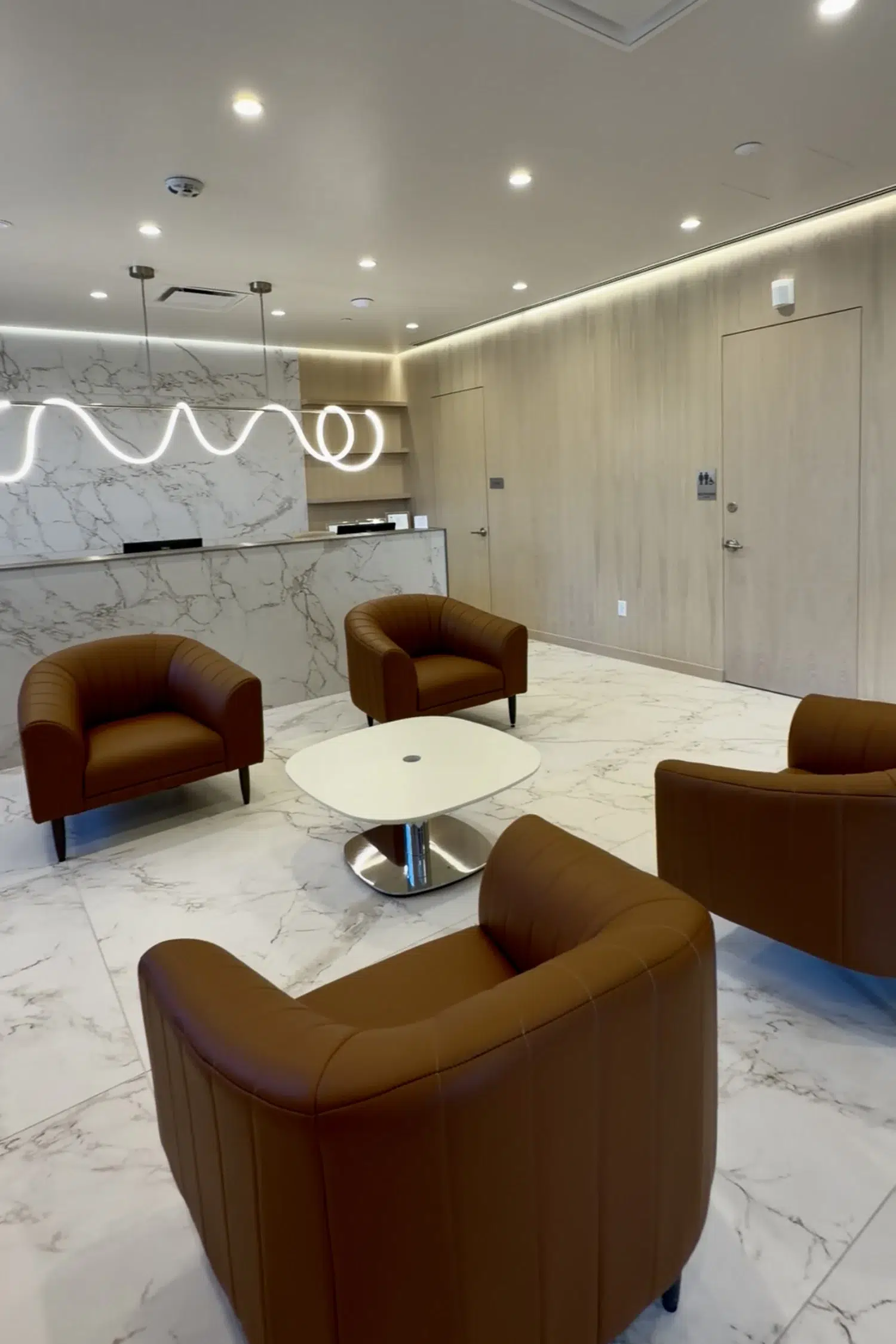 Modern surgical center waiting room with white marble floors, cognac leather chairs, and a unique neon light fixture.