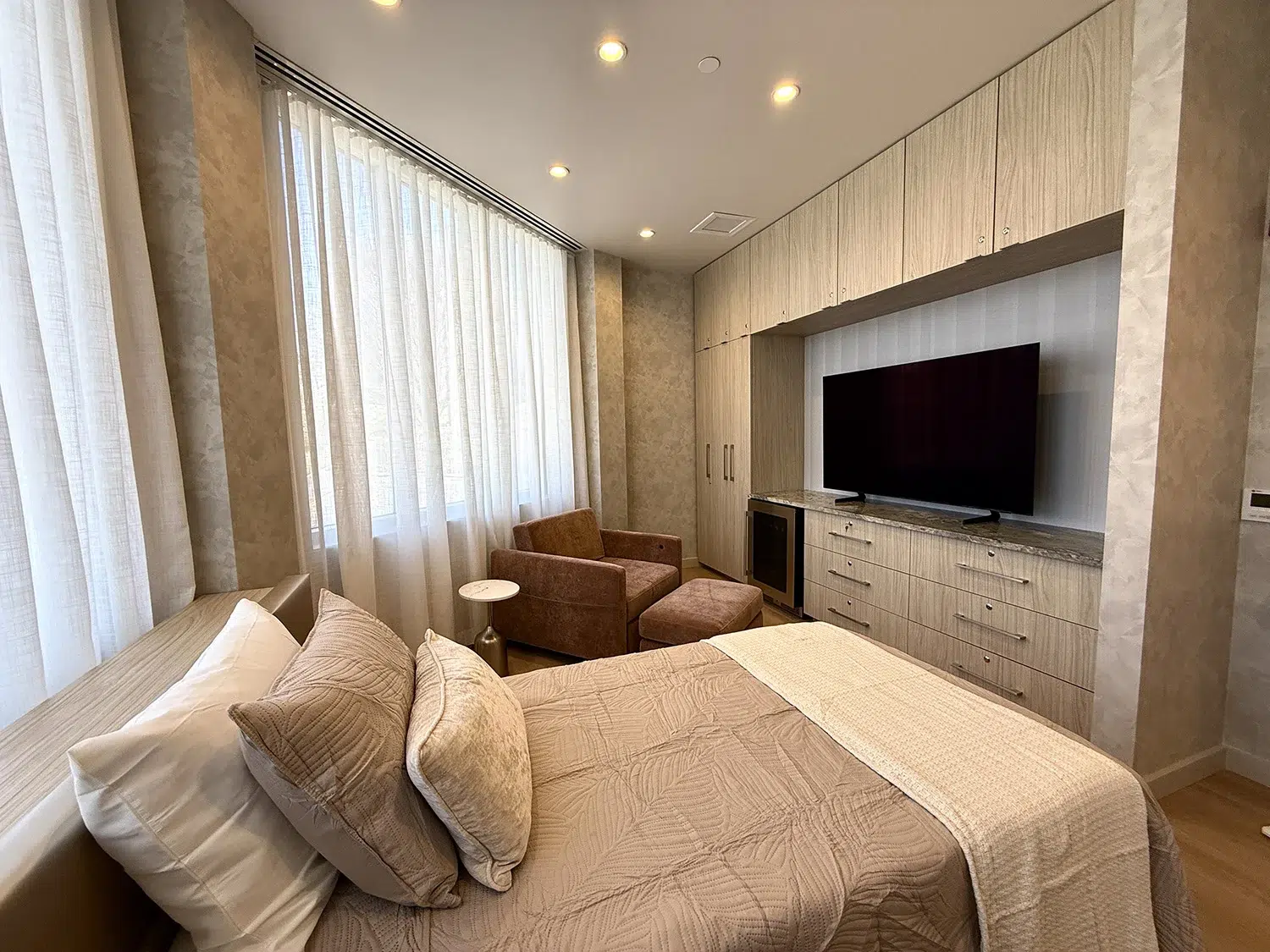 Luxury patient recovery suite featuring a large wall-mounted TV, custom cabinetry, and a plush lounge chair with ottoman.