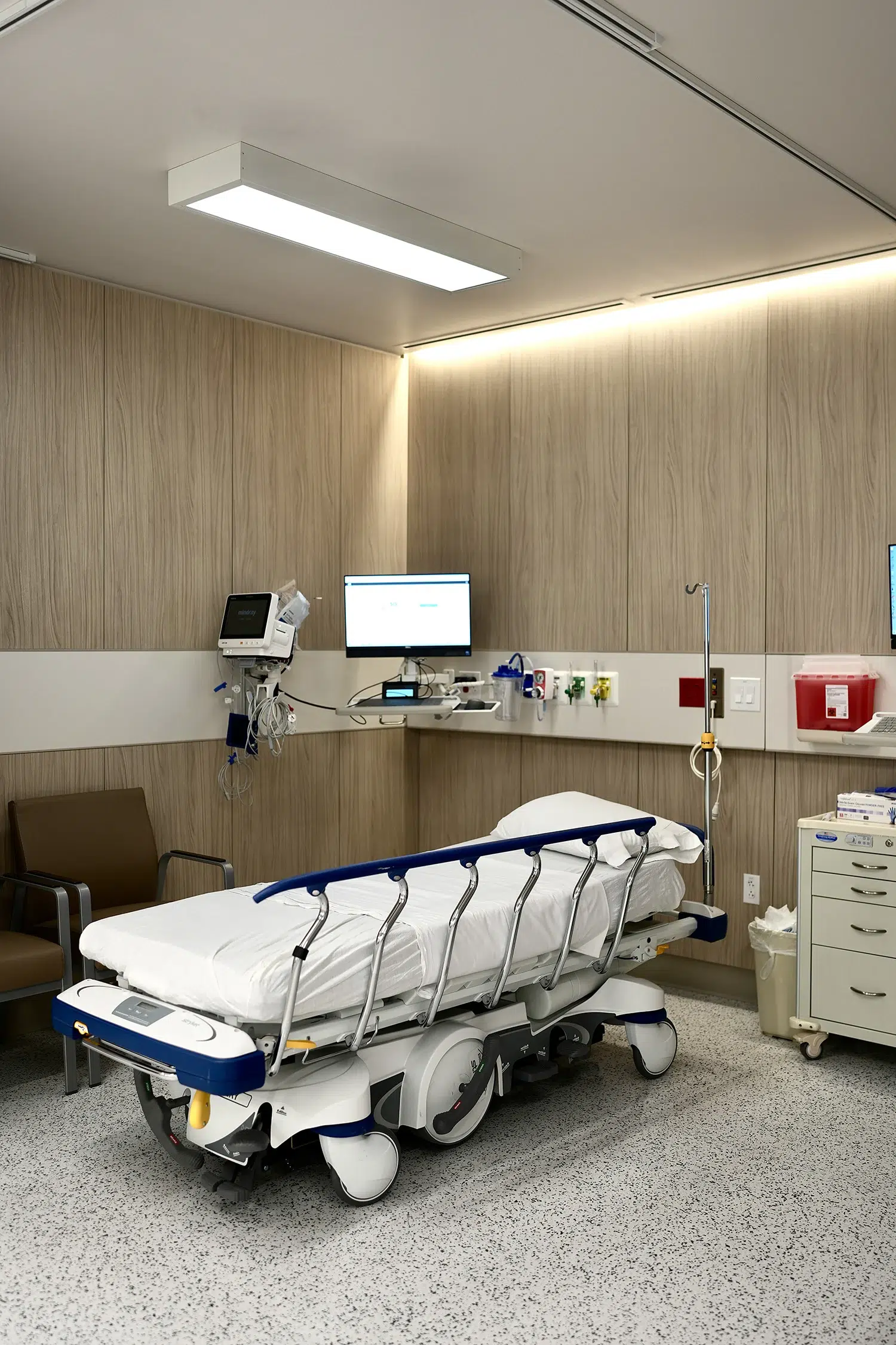 Modern post-op recovery room with Stryker medical bed, wood paneling, and patient monitoring equipment.
